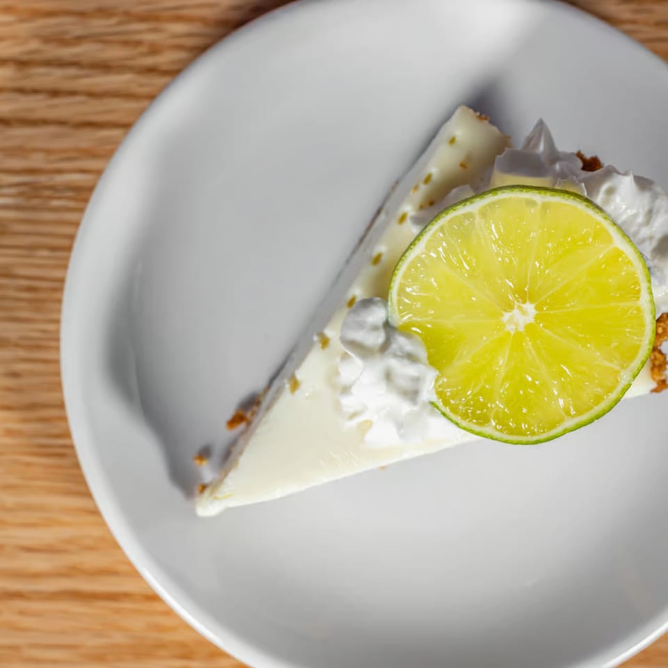 Slice of key lime pie with whipped cream and a lime slice on a white plate.