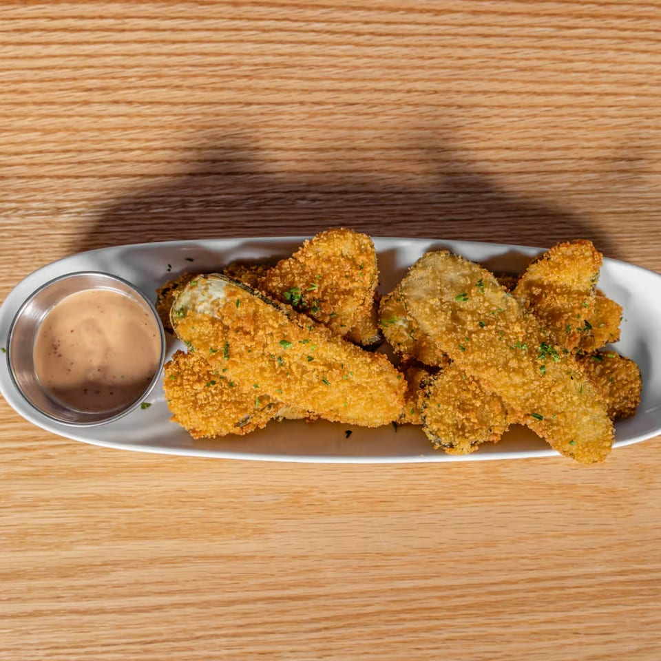 Crispy fried pickles with a side of creamy dipping sauce on a white plate.