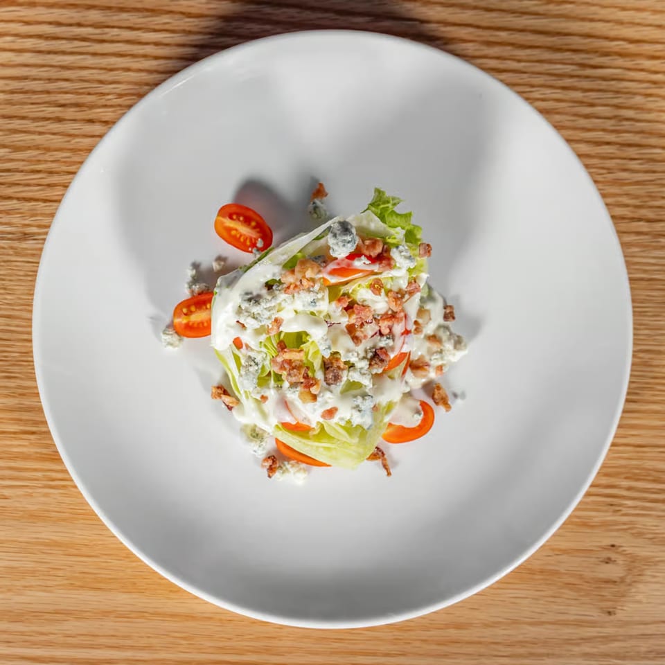 Wedge salad with blue cheese dressing, bacon bits, and cherry tomatoes on a white plate.