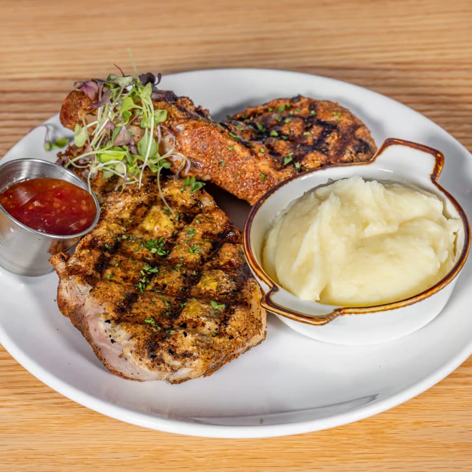 Grilled pork chops with mashed potatoes and a side of sweet chili sauce on a white plate.