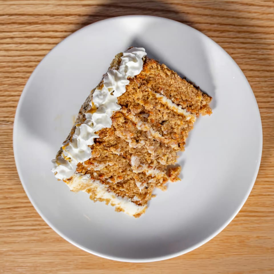Slice of carrot cake with white frosting and whipped cream on a white plate.
