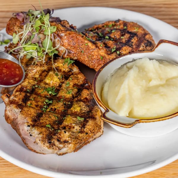 Grilled pork chops with mashed potatoes and a side of sweet chili sauce on a white plate.