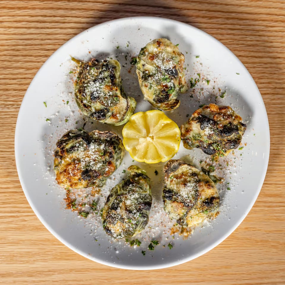 Six baked artichoke hearts topped with cheese and herbs, surrounding a lemon half on a white plate.