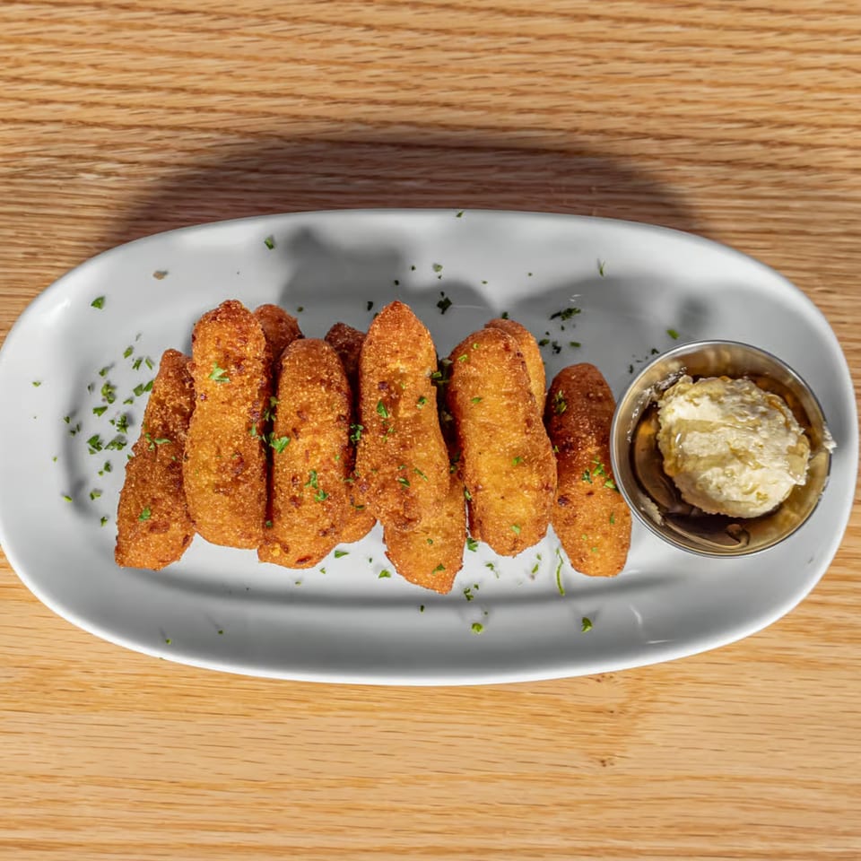 Golden-brown fried hush puppies with parsley flakes and a side of honey butter on a white plate.