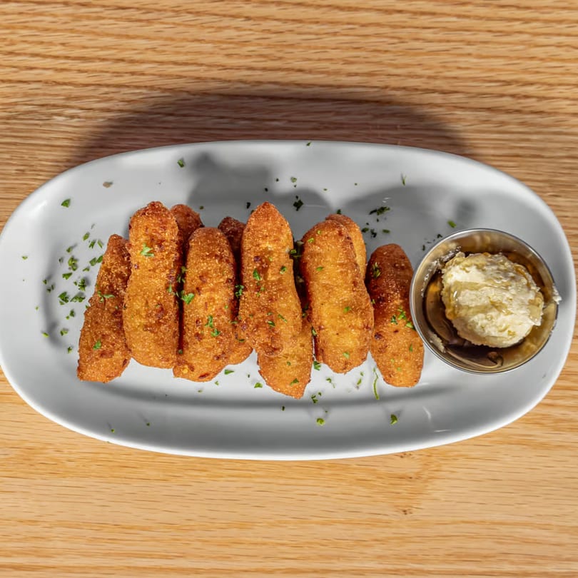 Golden-brown fried hush puppies with parsley flakes and a side of honey butter on a white plate.